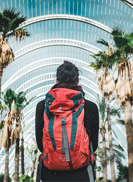 Woman with dark hair in a bun wearing a red backpack facing away from the camera